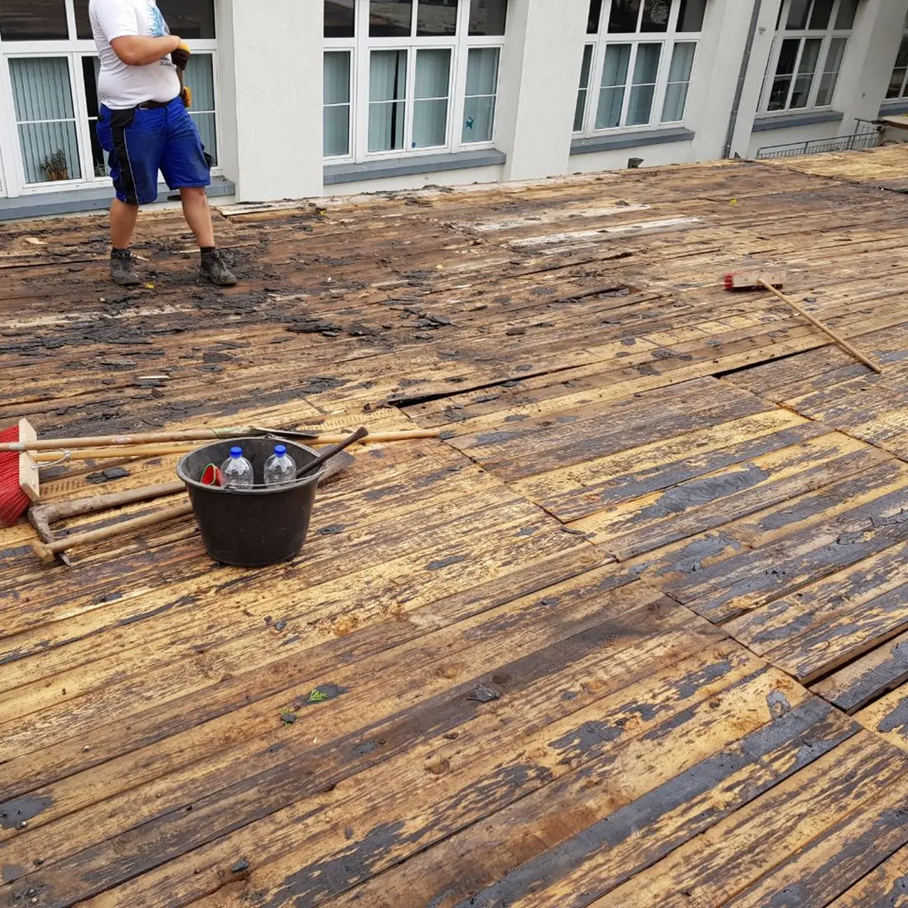 Eine große Terrasse mit abgetragenen Holzdielen, daneben Besen, Schaufeln und ein Mörtelkübel